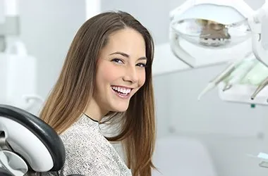 Woman smiling in dental office chair with equipment visible in background.