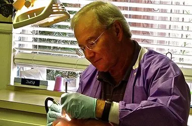 Dentist in purple shirt examining patient's teeth in dental office setting.