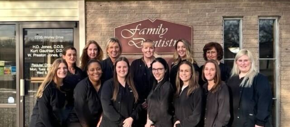 Team of dental professionals posing together outside Gauthier & Jones Family Dentistry office entrance.